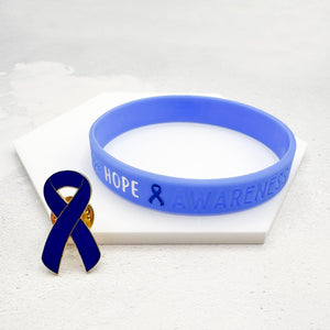 blue silicone awareness ribbon wristband with "Hope & Awareness" text engraved on its side, and a blue enamel ribbon pin on a white surface