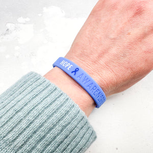 blue silicone awareness ribbon wristband with "Hope & Awareness" text engraved on its side worn on a person's wrist