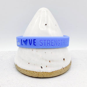 blue silicone awareness ribbon wristband with "love strength" text engraved on its side 