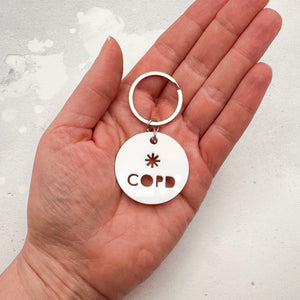 lightweight white acrylic round keychain with 'COPD' laser cut out, held in a hand