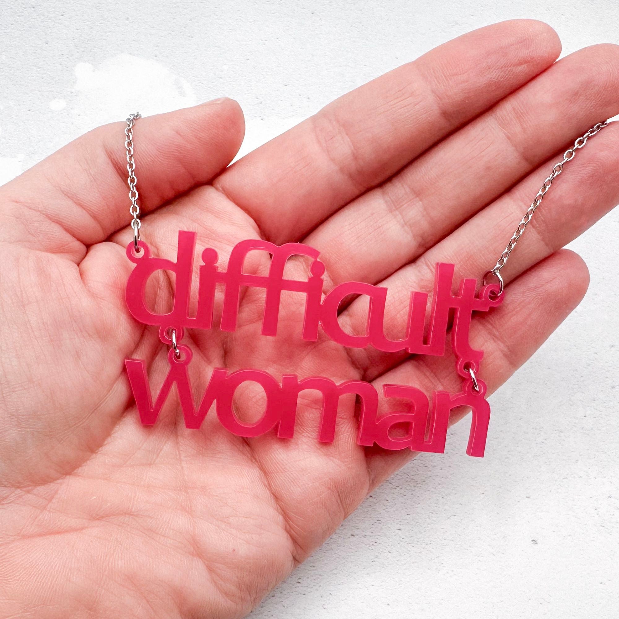 hot pink acrylic necklace which reads 'difficult woman' on a stainless steel chain held in a hand