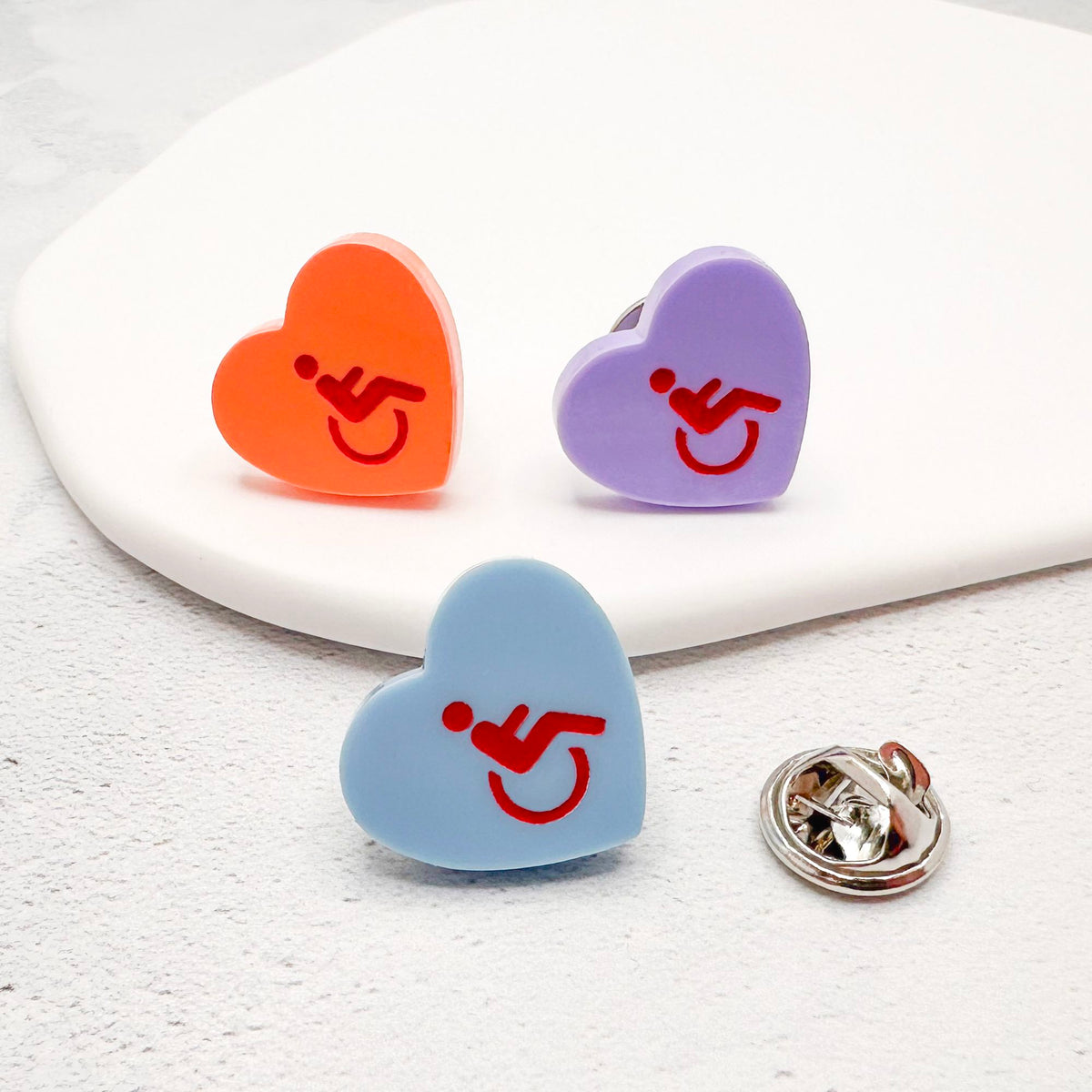 three acrylic heart pins with disabled symbol in red