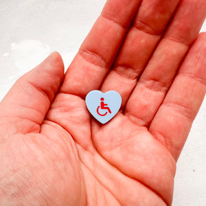 blue acrylic heart pin with disabled symbol in red held in hand