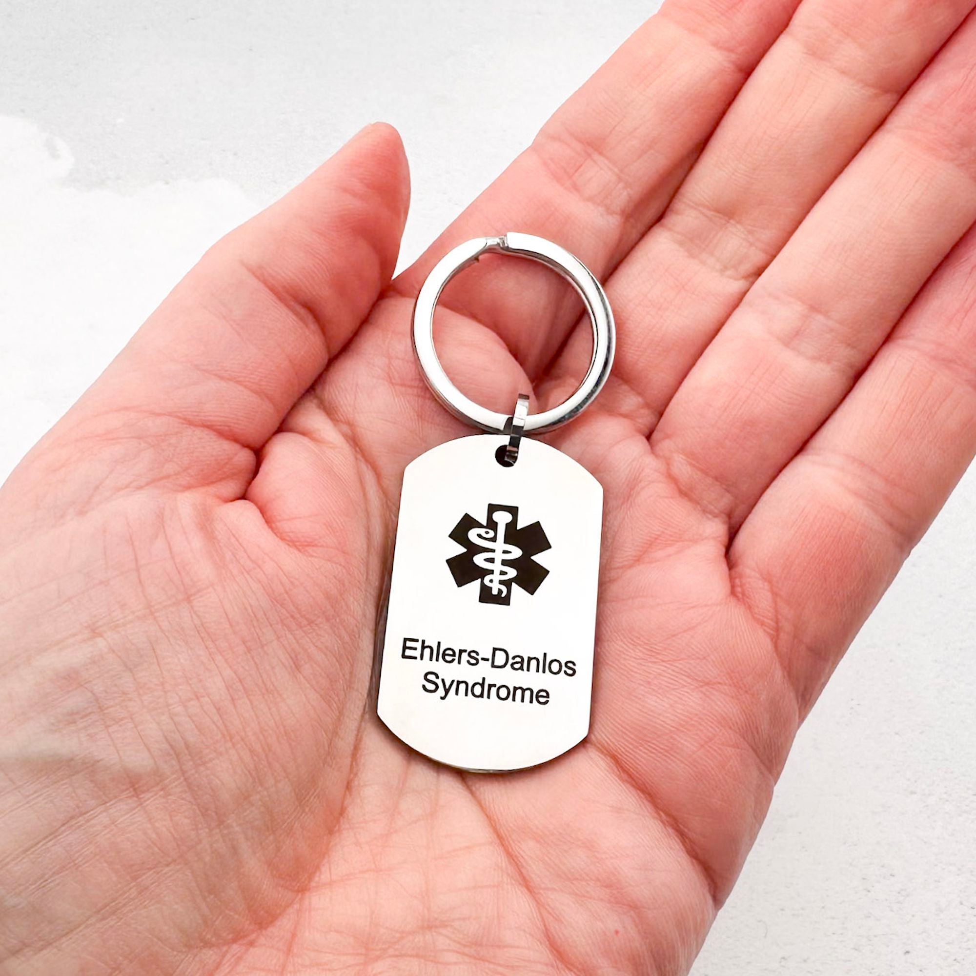 stainless steel keychain with star of life medical symbol and 'Ehlers-Danlos Syndrome' text held in hand