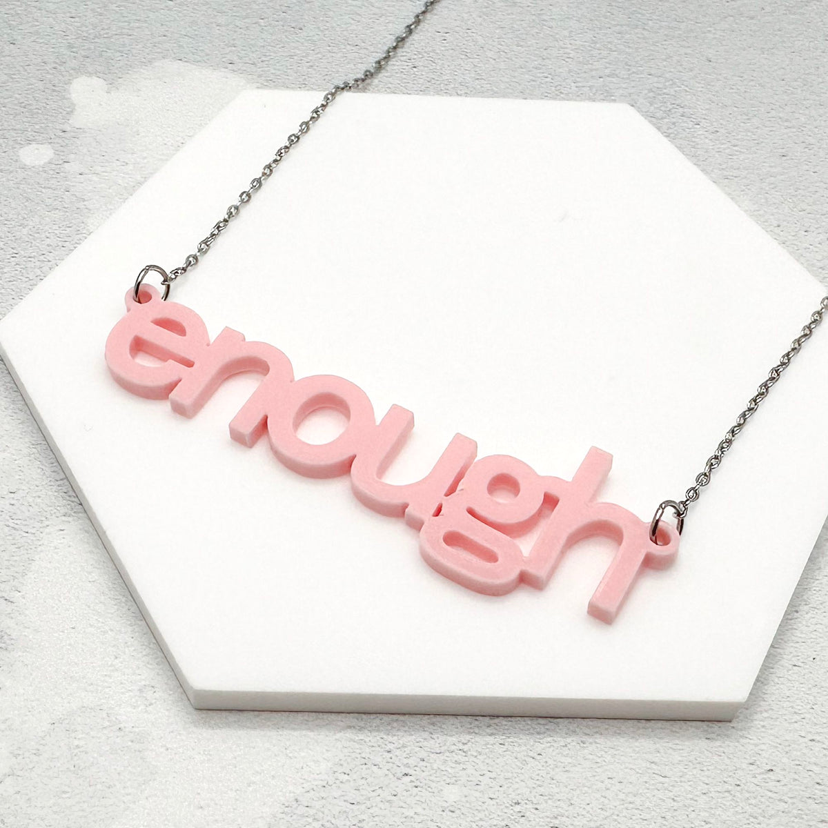 Flat lay of soft pink acrylic “enough” necklace on white background