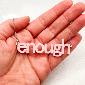 Soft pink acrylic “enough” word necklace with stainless steel chain held in hand