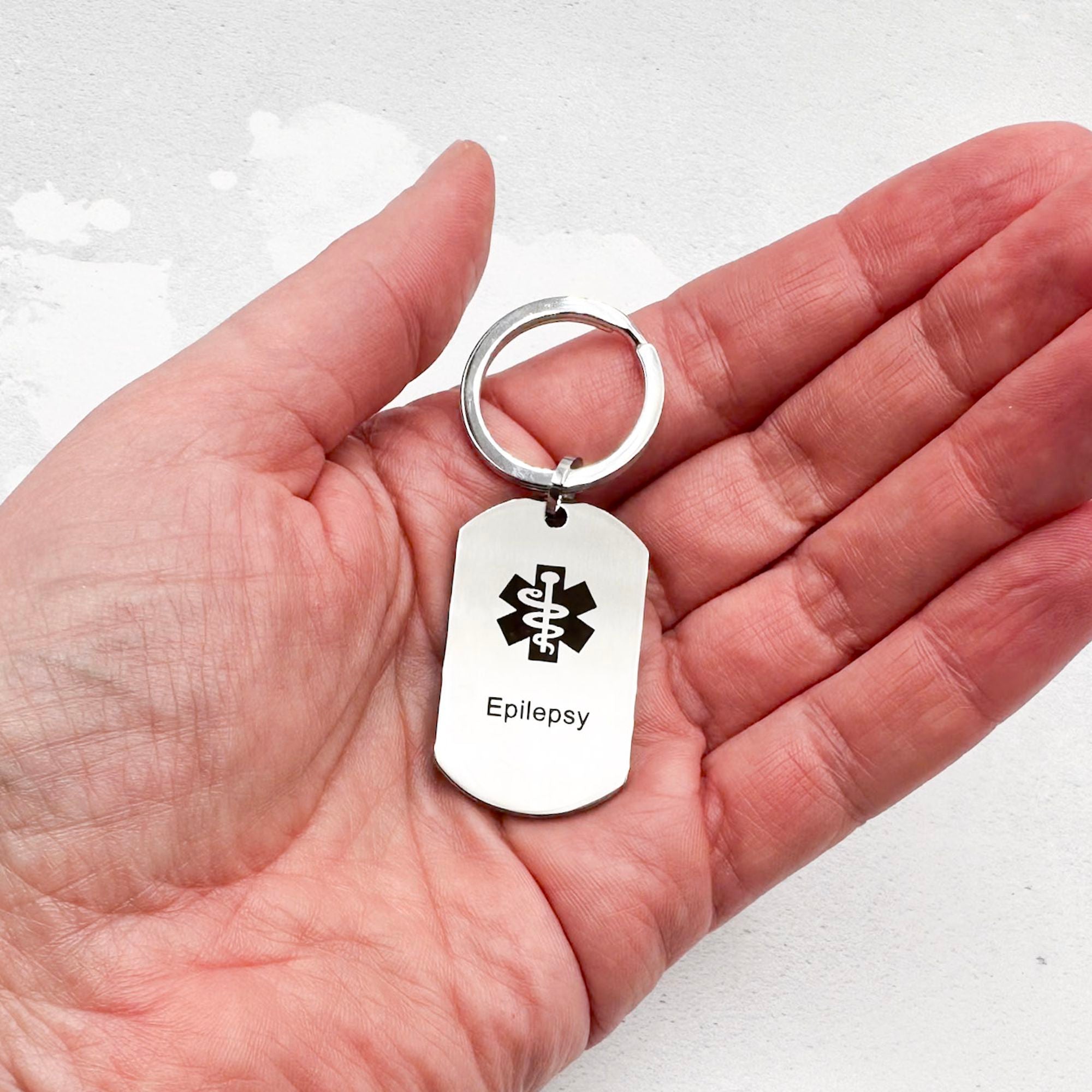 stainless steel keychain with star of life medical symbol and 'Epilepsy' text held in hand