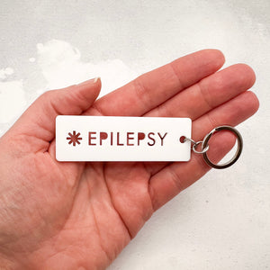 Acrylic epilepsy medical alert keychain with laser-cut text and silver keyring held in hand