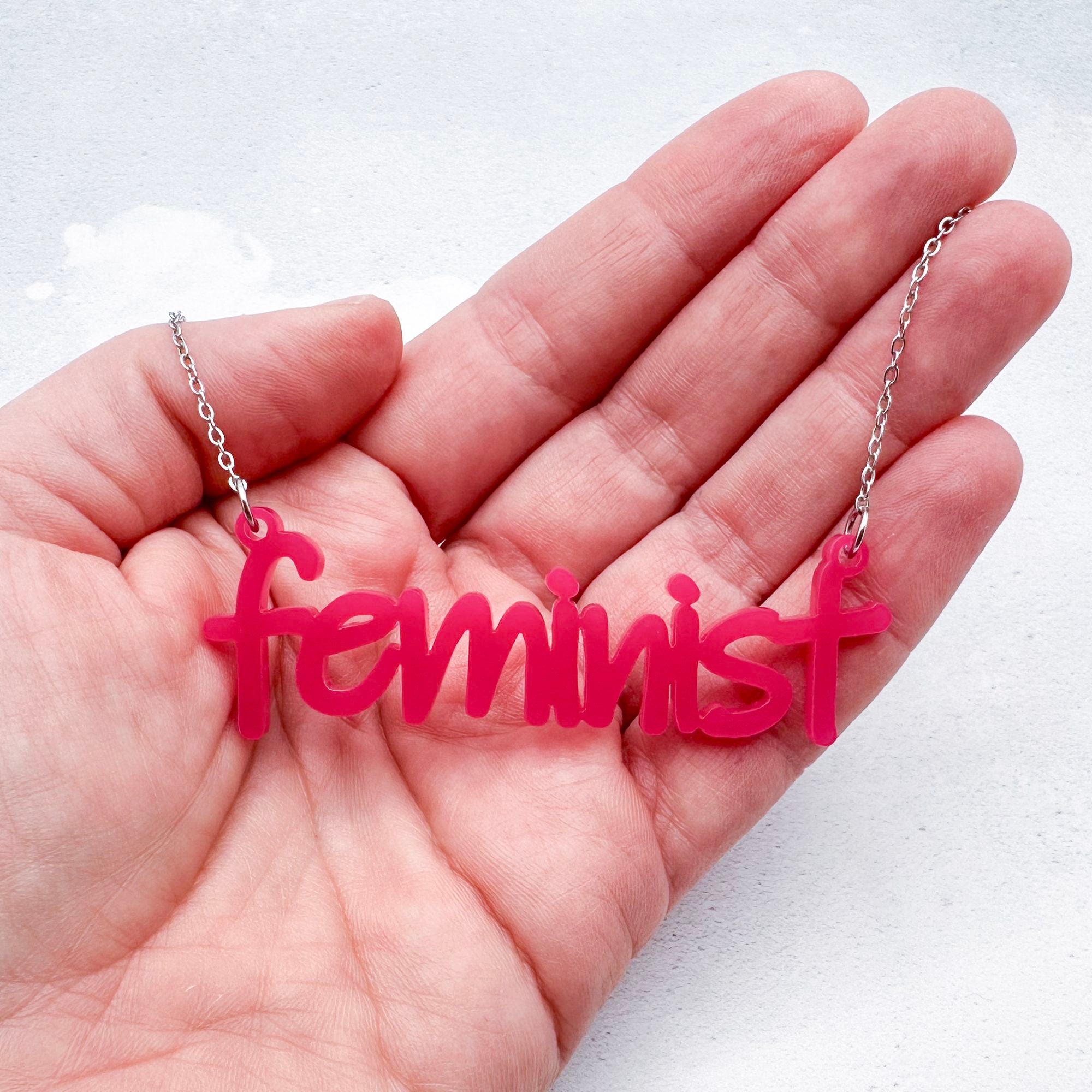 hot pink acrylic feminist necklace on a stainless steel chain held in a hand