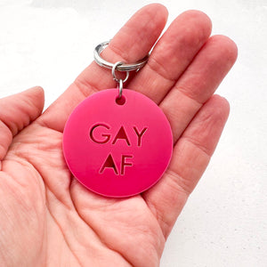 round hot pink acrylic keychain with 'GAY AF' text held in hand