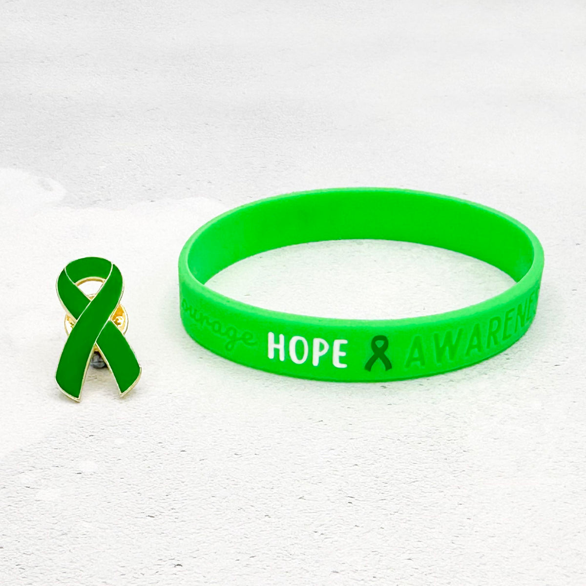 green awareness ribbon wristband with "hope & awareness" text engraved on the side and a matching green enamel ribbon pin besides it