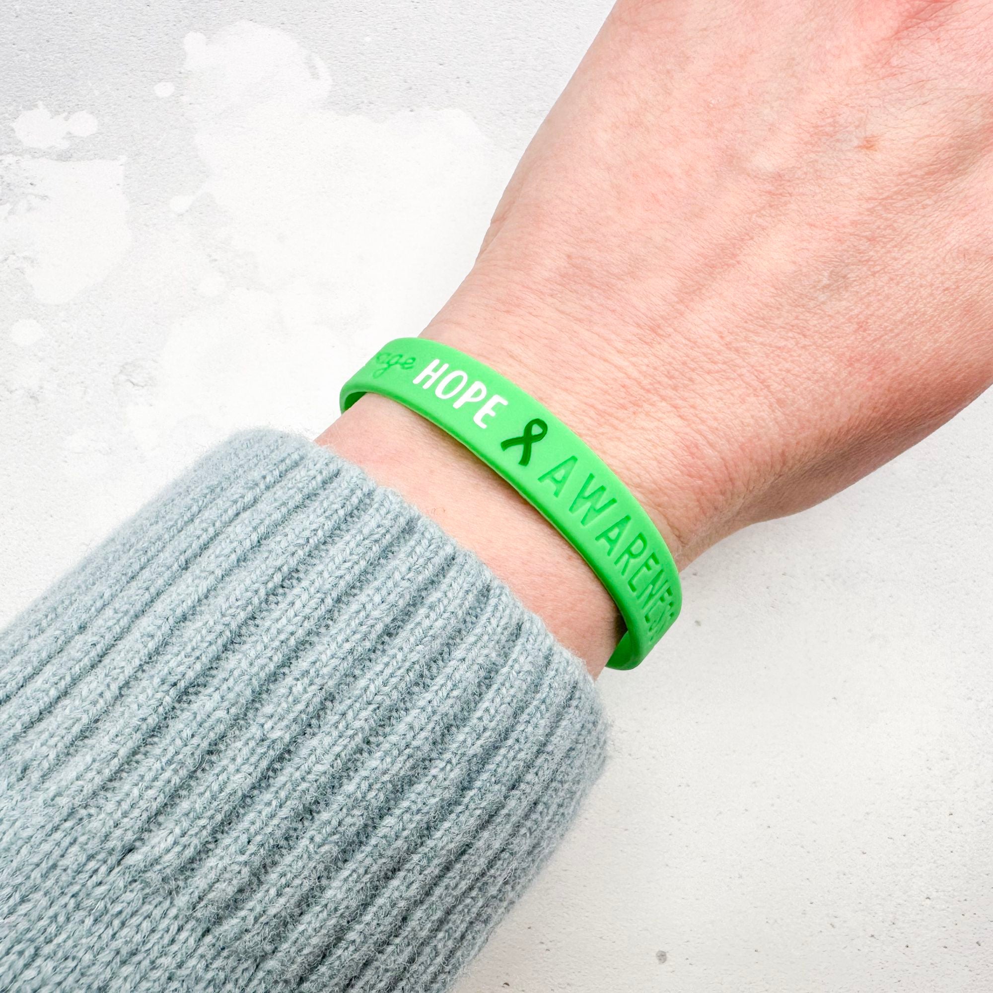green awareness ribbon wristband with "hope & awareness" text engraved on the side worn on a person's wrist