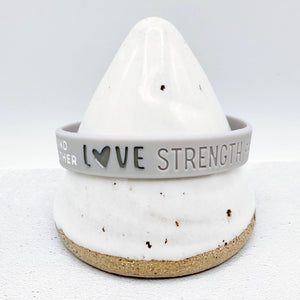 grey awareness ribbon wristband with "love strength" text engraved on its side 