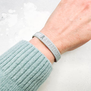 grey awareness ribbon wristband with "hope & awareness" text engraved on its side worn on a person's wrist