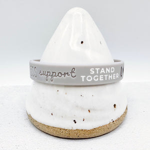 grey awareness ribbon wristband with "support stand together" text engraved on its side 