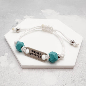 white nylon cord bracelets with two teal blue geometric beads either side a stainless steel tag engraved with grid coordinates