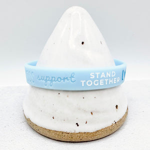 light blue awareness ribbon wristband with "support stand together" text engraved on its side 