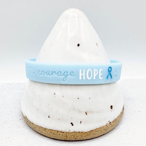 light blue awareness ribbon wristband with "courage hope" text engraved on its side 