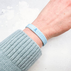 light blue awareness ribbon wristband with "hope & awareness" text engraved on its side on a person's wrist