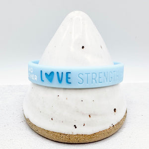 light blue awareness ribbon wristband with "love strength" text engraved on its side 
