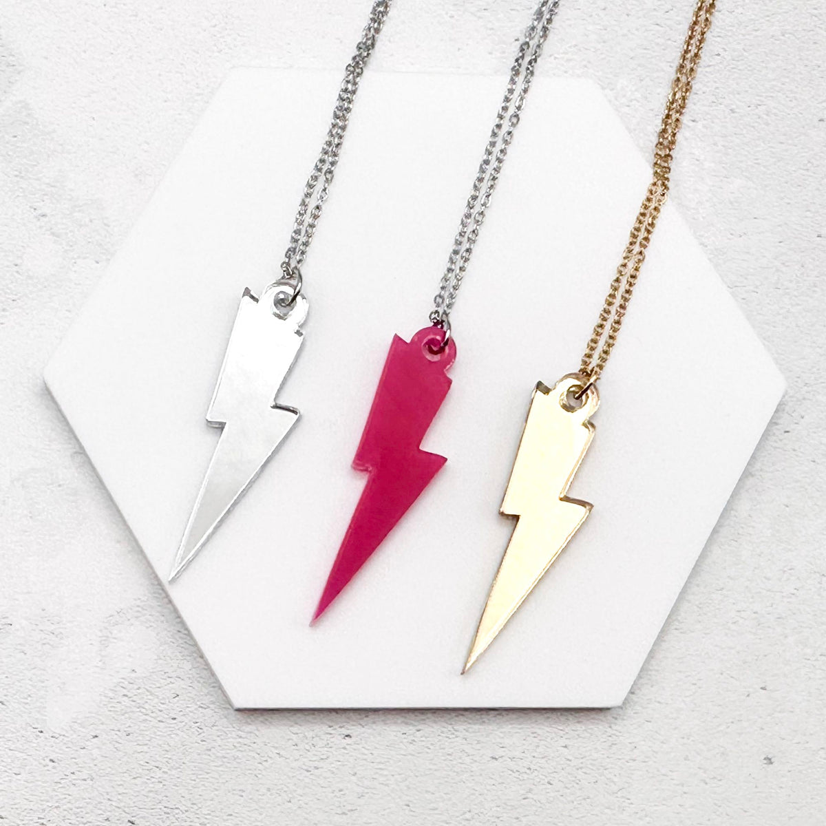 Three necklaces with lightning bolt pendants on a white background