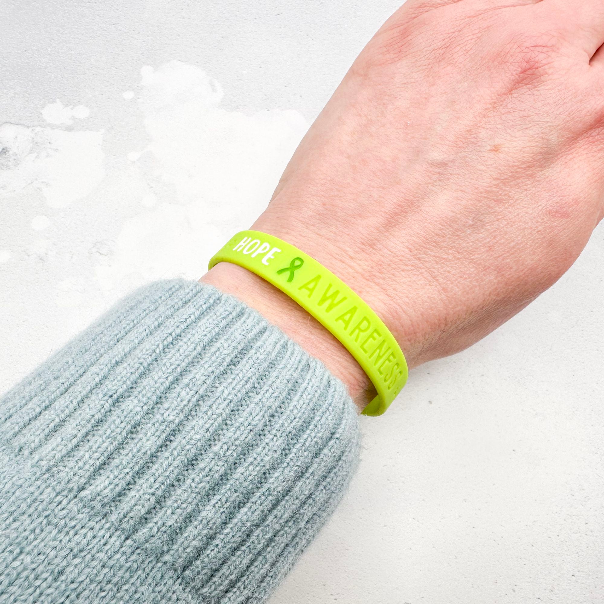 Lime green silicone wristband engraved with ‘Hope & Awareness’ worn on person's wrist