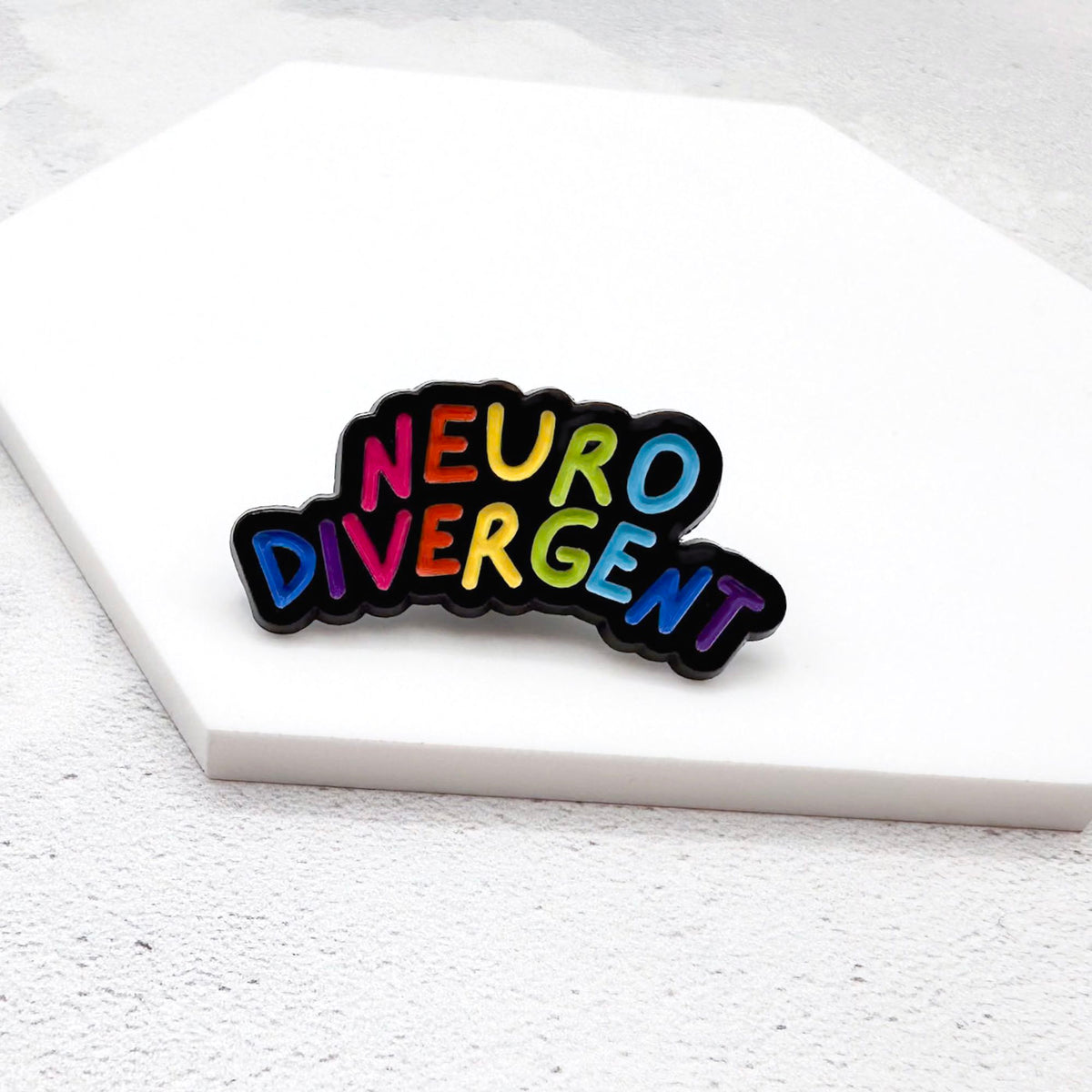 enamel pin with "Neurodivergent" in rainbow lettering