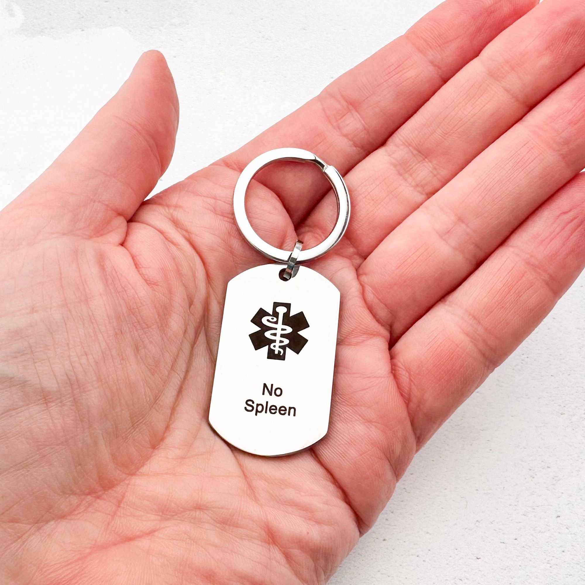 stainless steel keychain with star of life medical symbol and 'No Spleen' text held in hand