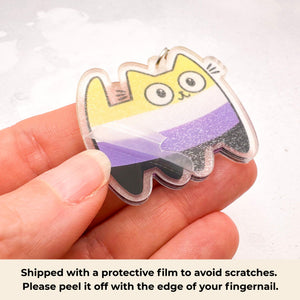 A cute acrylic keychain shaped like a cartoon cat in the nonbinary flag colours and protective film