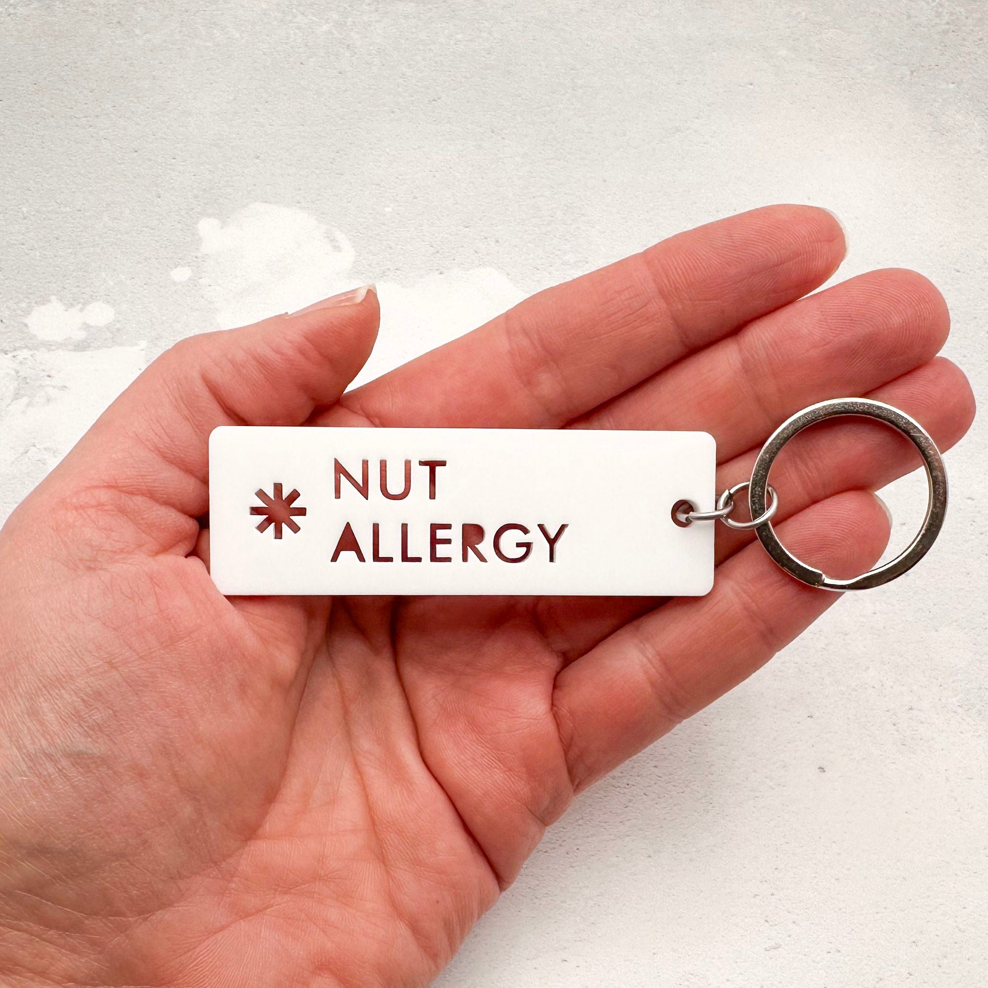 Acrylic nut allergy medical alert keychain with laser-cut text and silver keyring held in hand