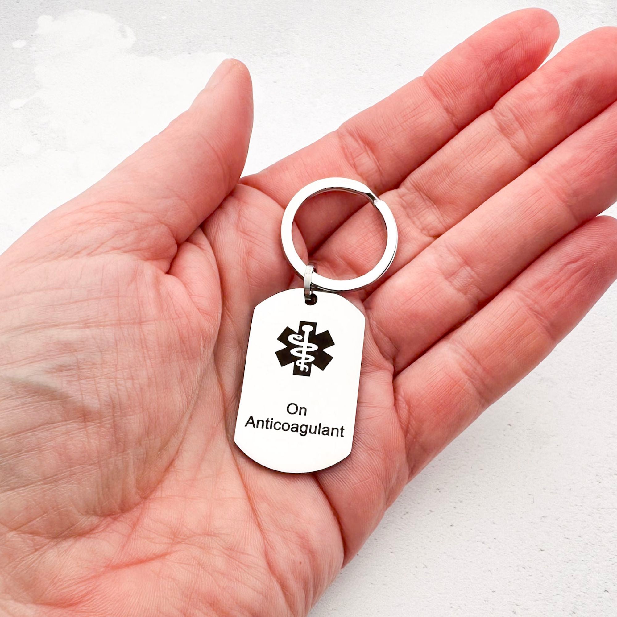 stainless steel keychain with star of life medical symbol and 'On Anticoagulant' text held in hand