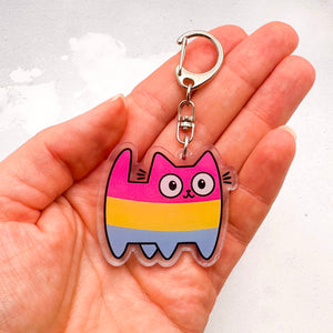 A hand holding a pansexual-striped cat keychain charm with a silver metal clasp