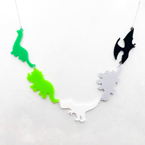 Necklace with five dinosaur-shaped pendants in the aromantic colours of green, light green, white, grey, and black, on a light grey background.