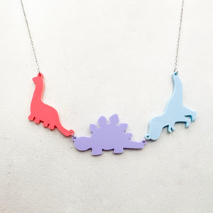 Necklace with three dinosaur-shaped pendants in pastel bisexual colours of pink, purple, and blue, on a light grey background.