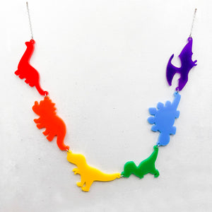 Necklace with six dinosaur-shaped pendants in the gay rainbow colours of red, orange, yellow, green, blue, and purple, on a light grey background.