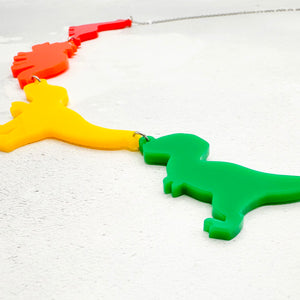 Necklace with dinosaur-shaped acrylic pendants in the gay rainbow colours on a light grey background.
