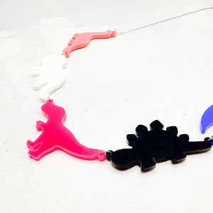 Necklace with dinosaur-shaped pendants in the genderfluid colours on a light grey background.