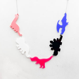 Necklace with five dinosaur-shaped pendants in genderfluid colours of pink, white, hot pink, black, and blue, on a light grey background.