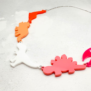Necklace with five dinosaur-shaped pendants in the lesbian colours on a textured grey background.