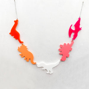 Necklace with five dinosaur-shaped pendants in the lesbian colours of orange, white, and pink on a light grey background.