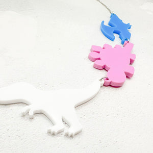 Necklace with dinosaur-shaped pendants in bold transgender colours on a light grey background