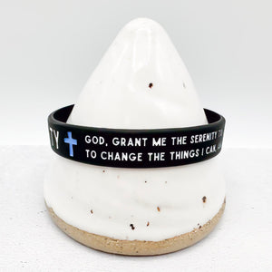 A black silicone bracelet with white text and a blue cross