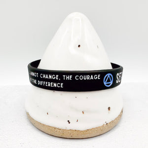 A black silicone wristband with white text and a blue circular symbol