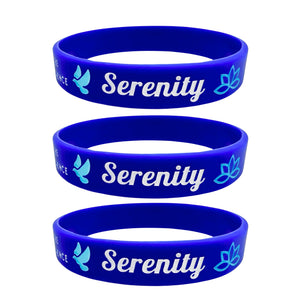 Three blue silicone wristbands stacked vertically, each printed with the word 'Serenity' in white script, a light blue dove, and a light blue lotus flower.