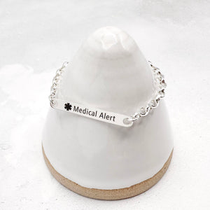 Silver medical alert bracelet on a white stand with a white background
