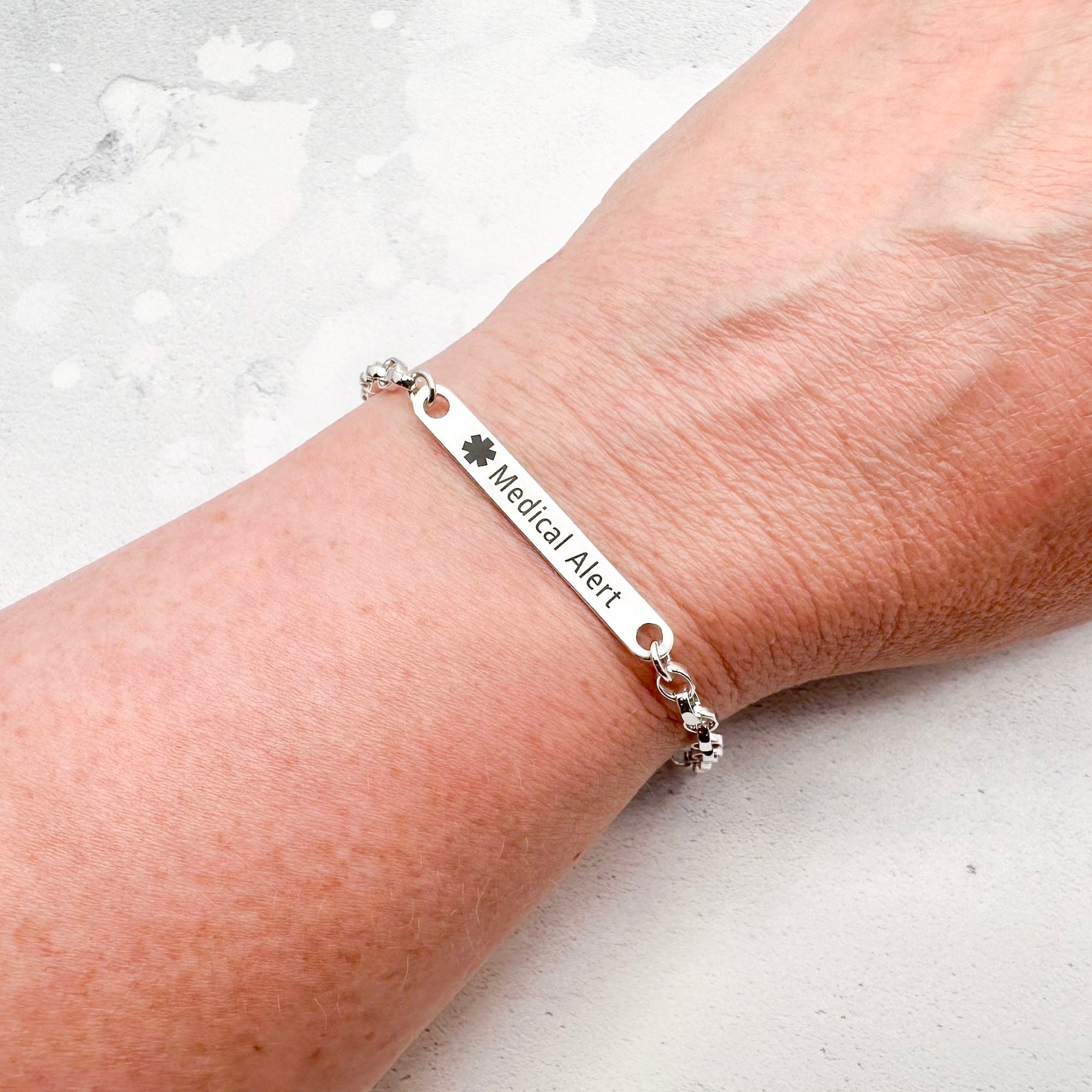 Silver medical alert bracelet on a wrist with a light background