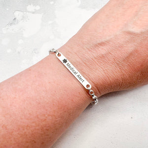 Silver medical alert bracelet on a wrist with a light background