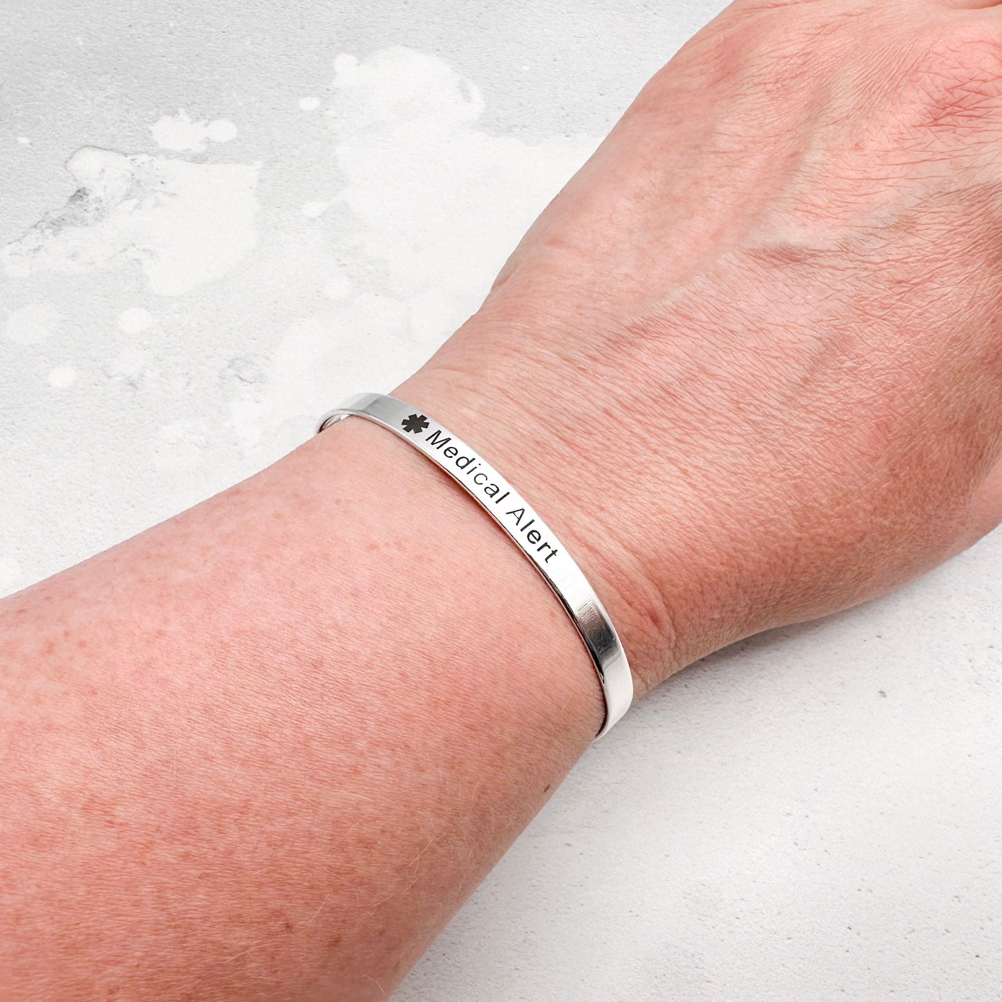Silver medical alert bracelet on a wrist against a light background