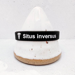 A black silicone wristband with white text reading 'Situs inversus' and a small medical symbol