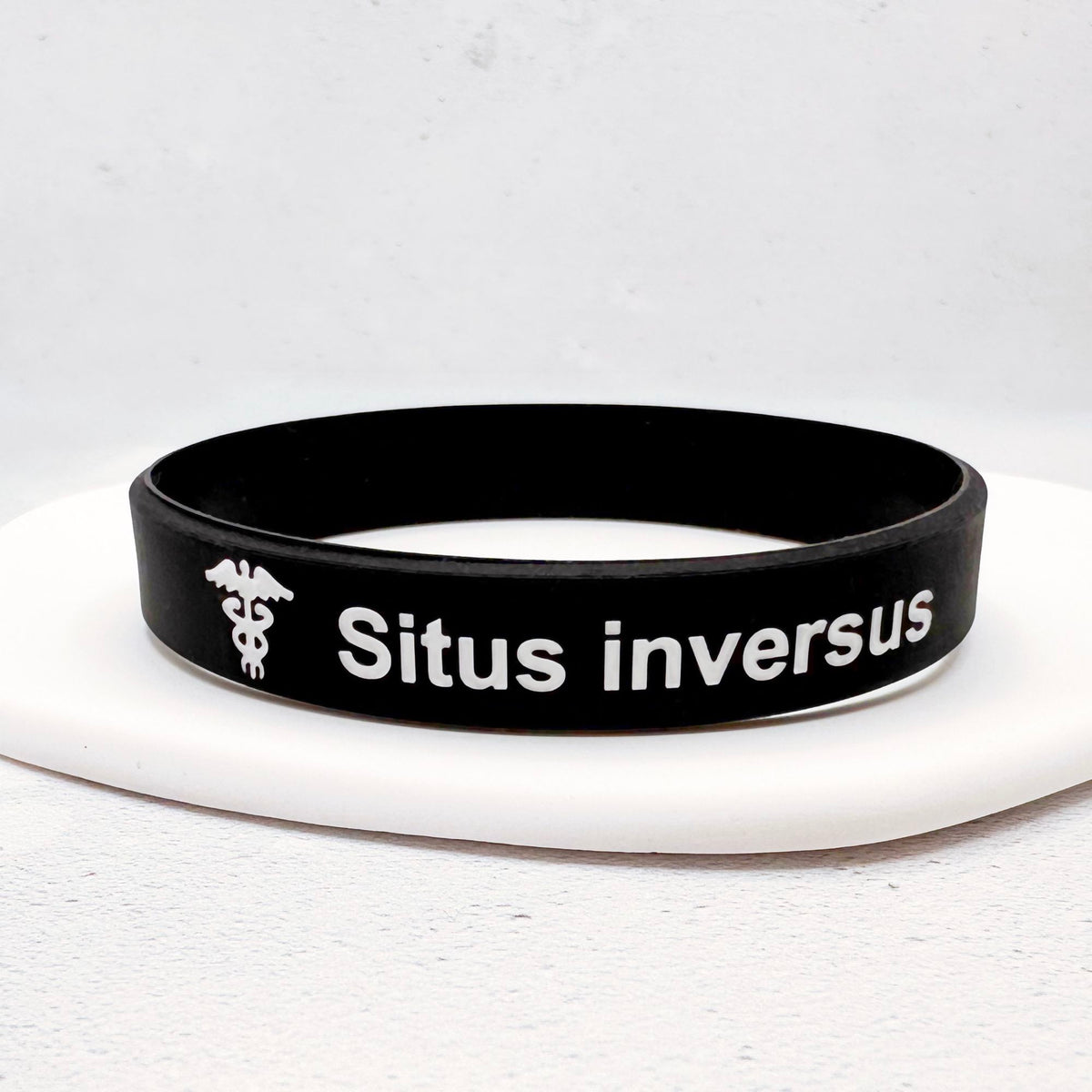 A black silicone wristband with white text reading 'Situs inversus' and a white caduceus symbol